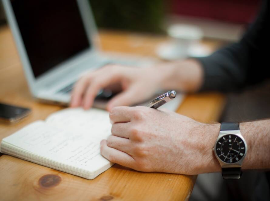 man sitting while writing on notebook